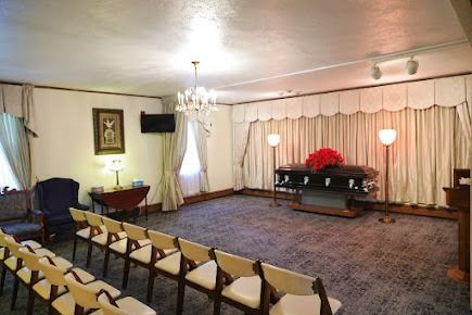 Funeral home interior with a casket, rows of chairs, and soft lighting.