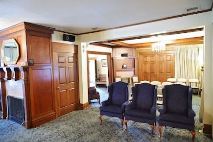 Funeral home waiting area with dark wood paneling, wingback chairs, and a fireplace.