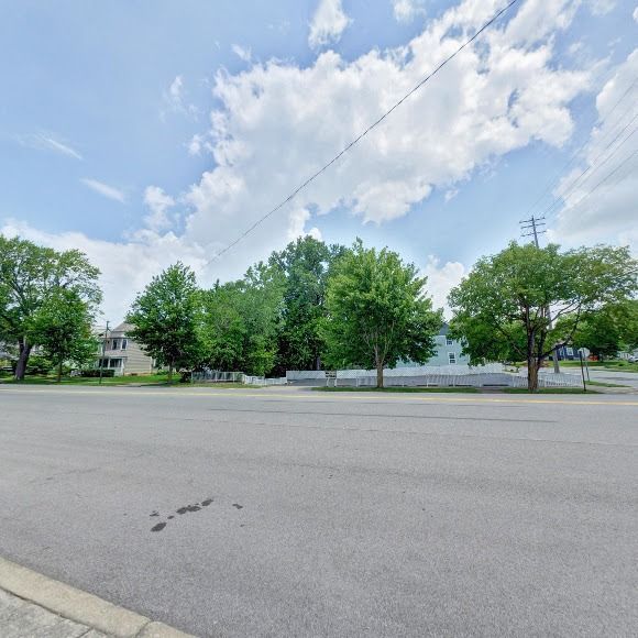 Paved road with trees and buildings under a partly cloudy sky.