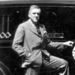 Man in suit leans against a car.