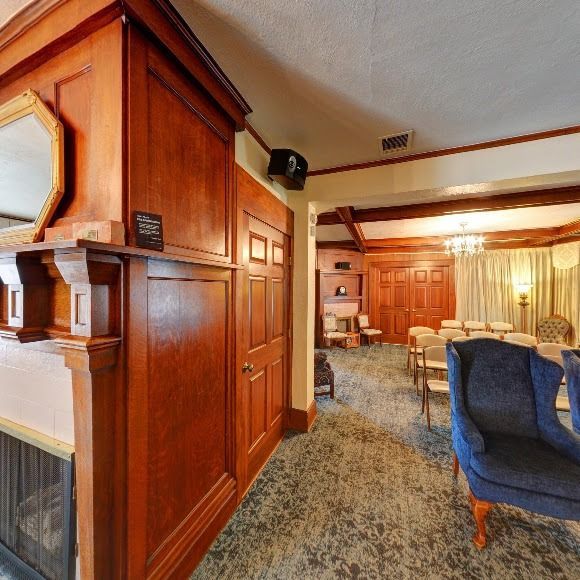 Wood-paneled room with fireplace, blue chairs, and rows of seating, likely for a ceremony or meeting.