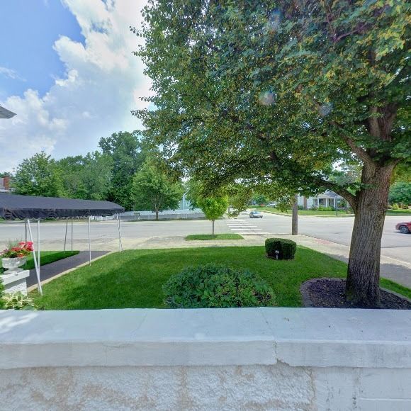 Exterior view of a building with a lawn, trees, and street on a sunny day.