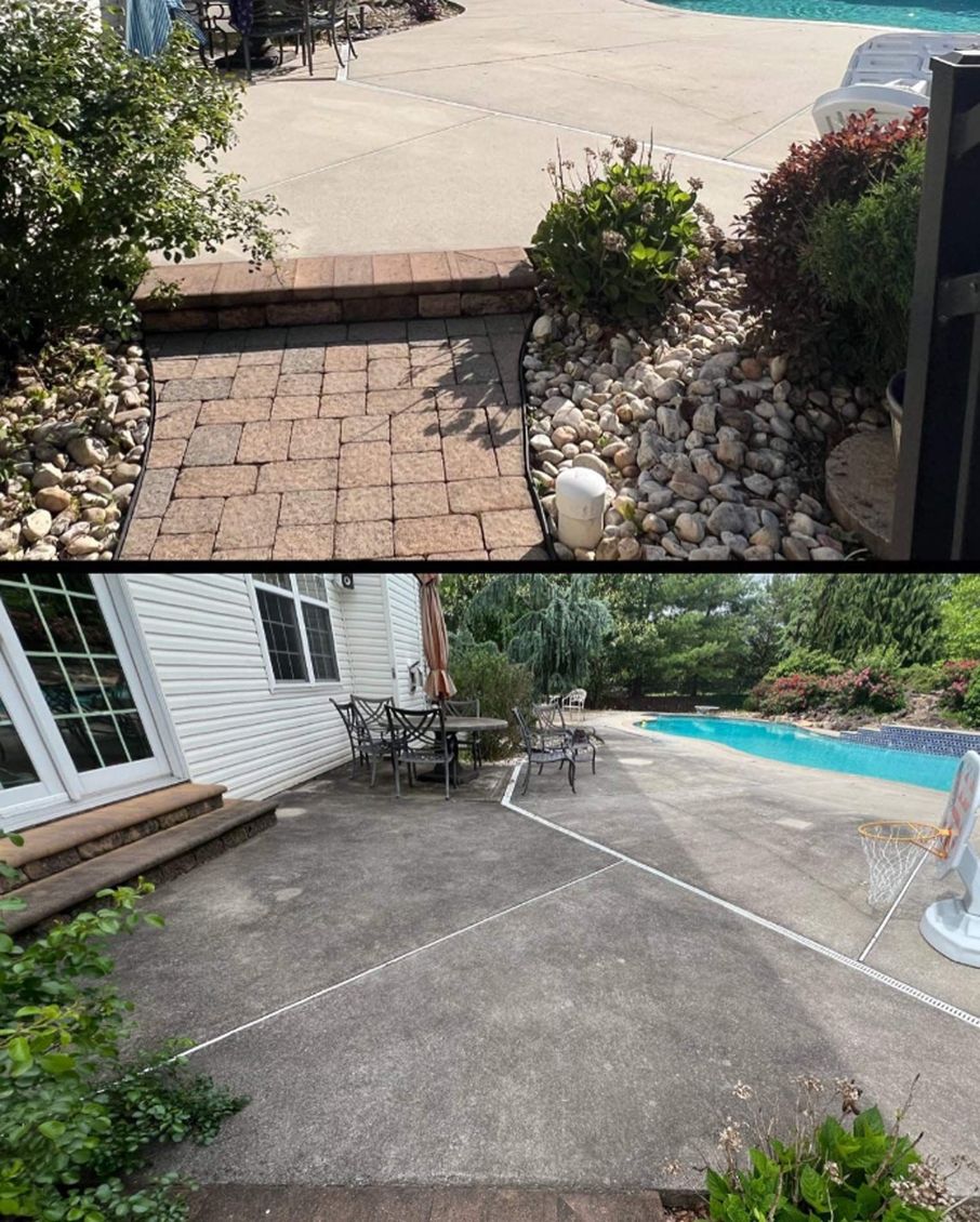Man wearing work clothes power washes a red brick patio next to a wooden shed. The backyard has green grass and flowering bushes.