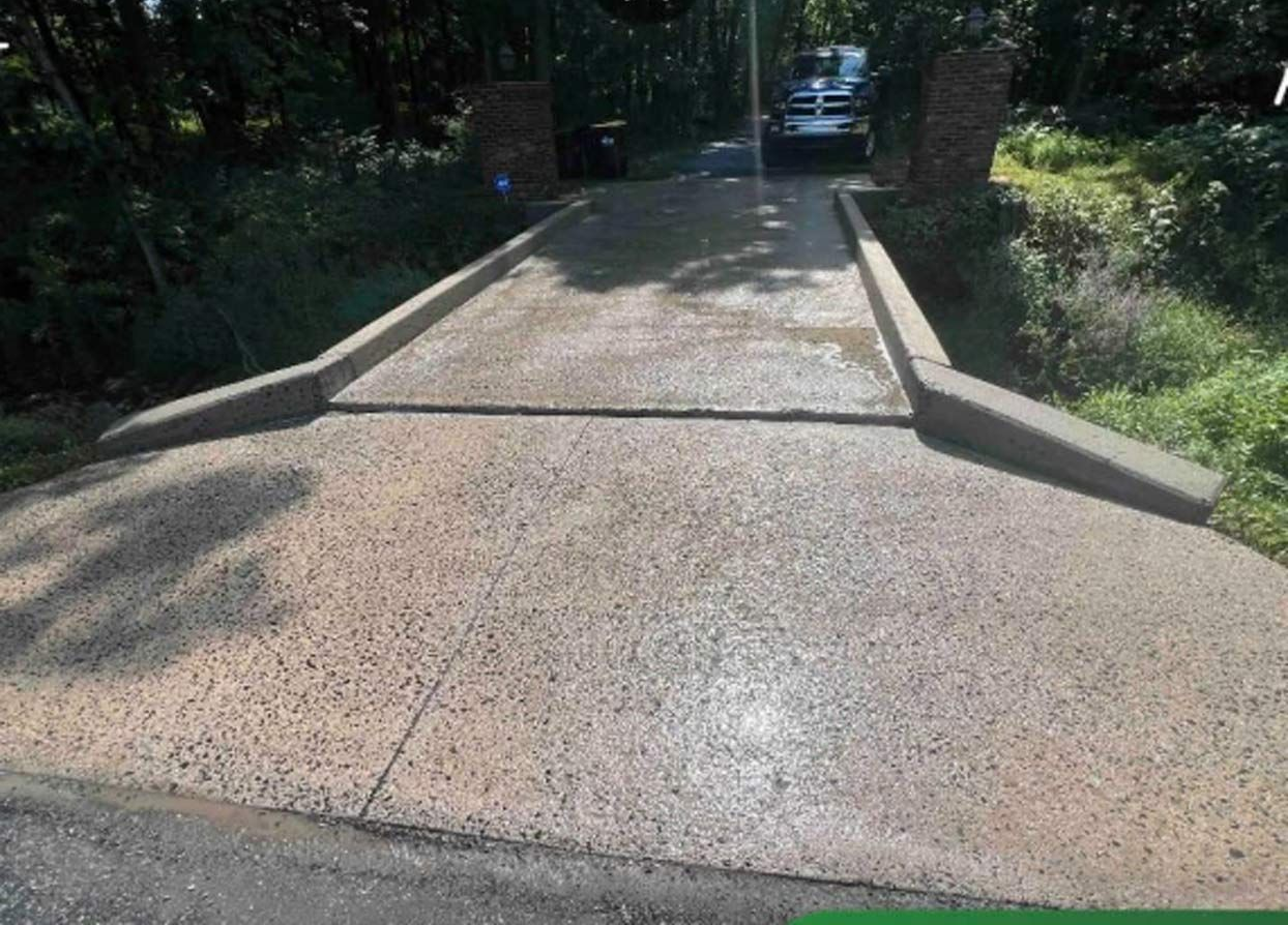 Person power washing a brick patio with a yellow pressure washer, wearing protective gear, in front of a house.