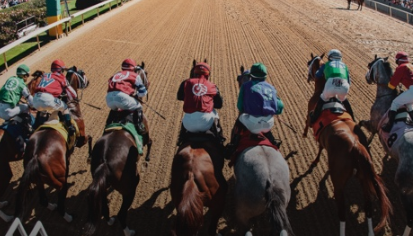 A group of jockeys are riding horses on a dirt track.