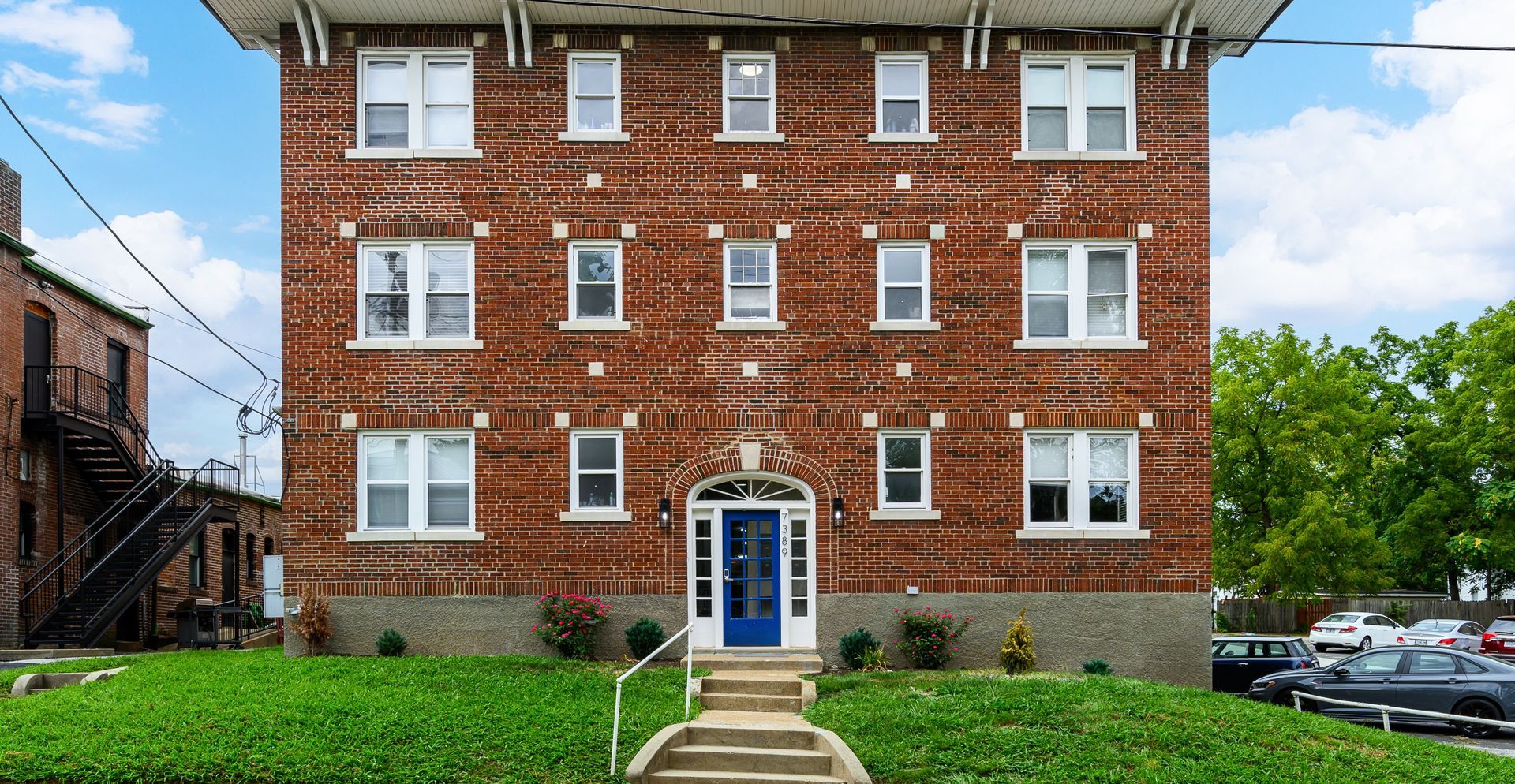 A large brick apartment building with a blue door and stairs leading to it.