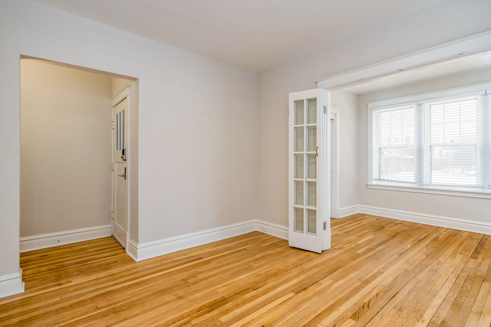 An empty living room with hardwood floors and white walls.