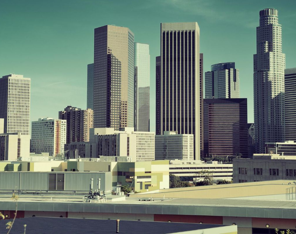 Downtown Los Angeles skyline, featuring various skyscrapers against a light teal sky.