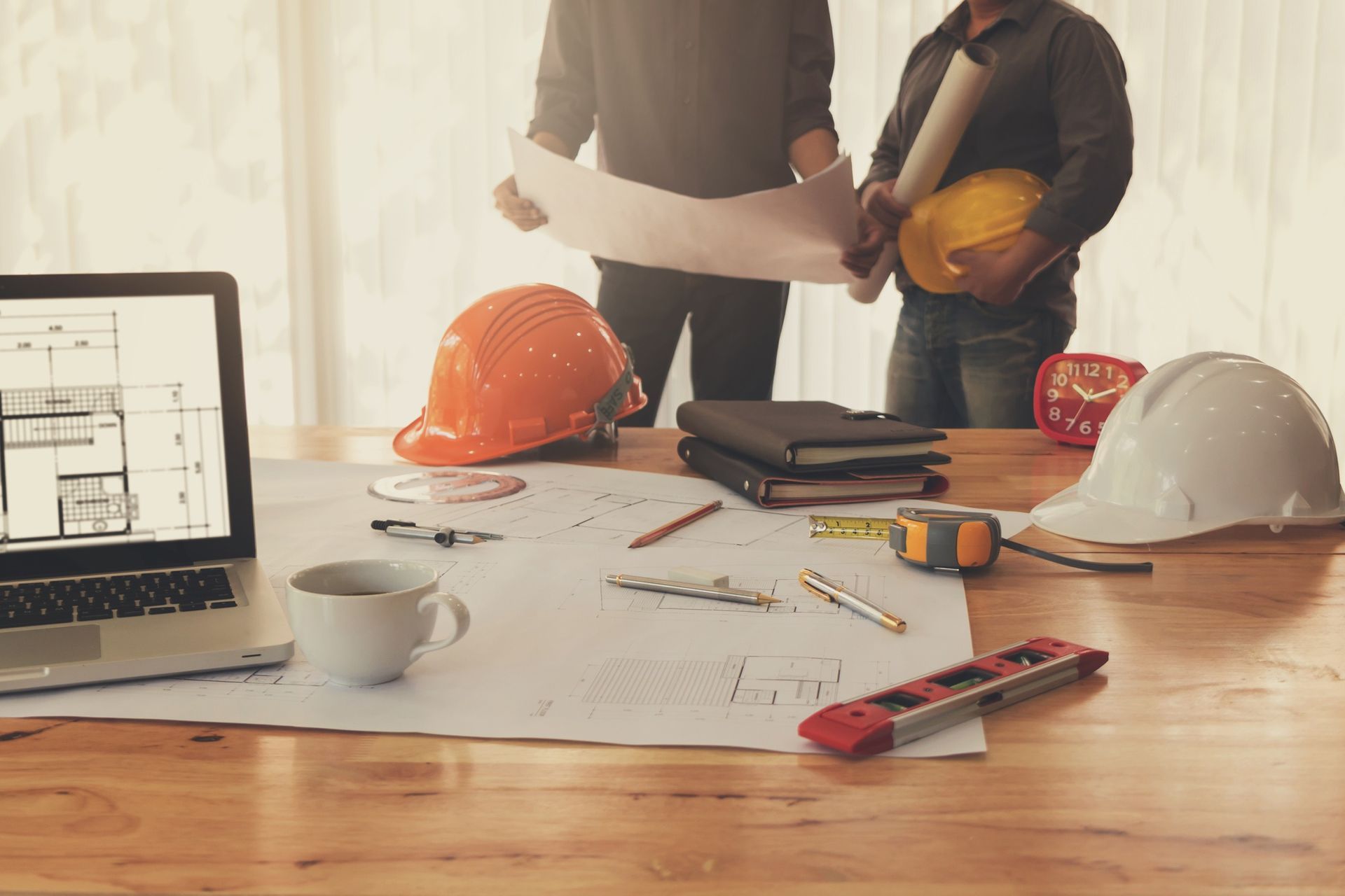 Engineers reviewing blueprints at a table with hard hats, a laptop, and tools.