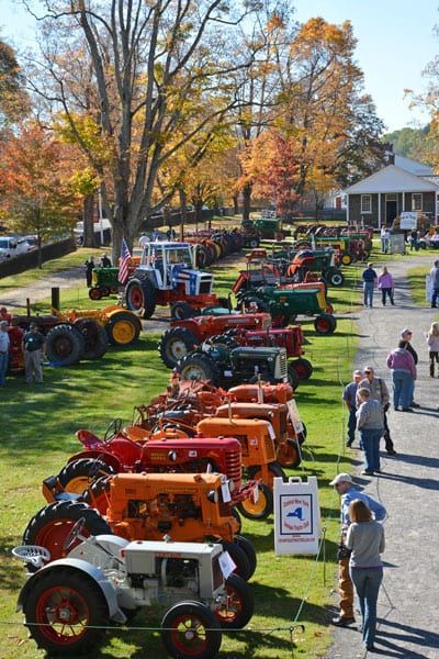 A row of old tractors are parked in a grassy field