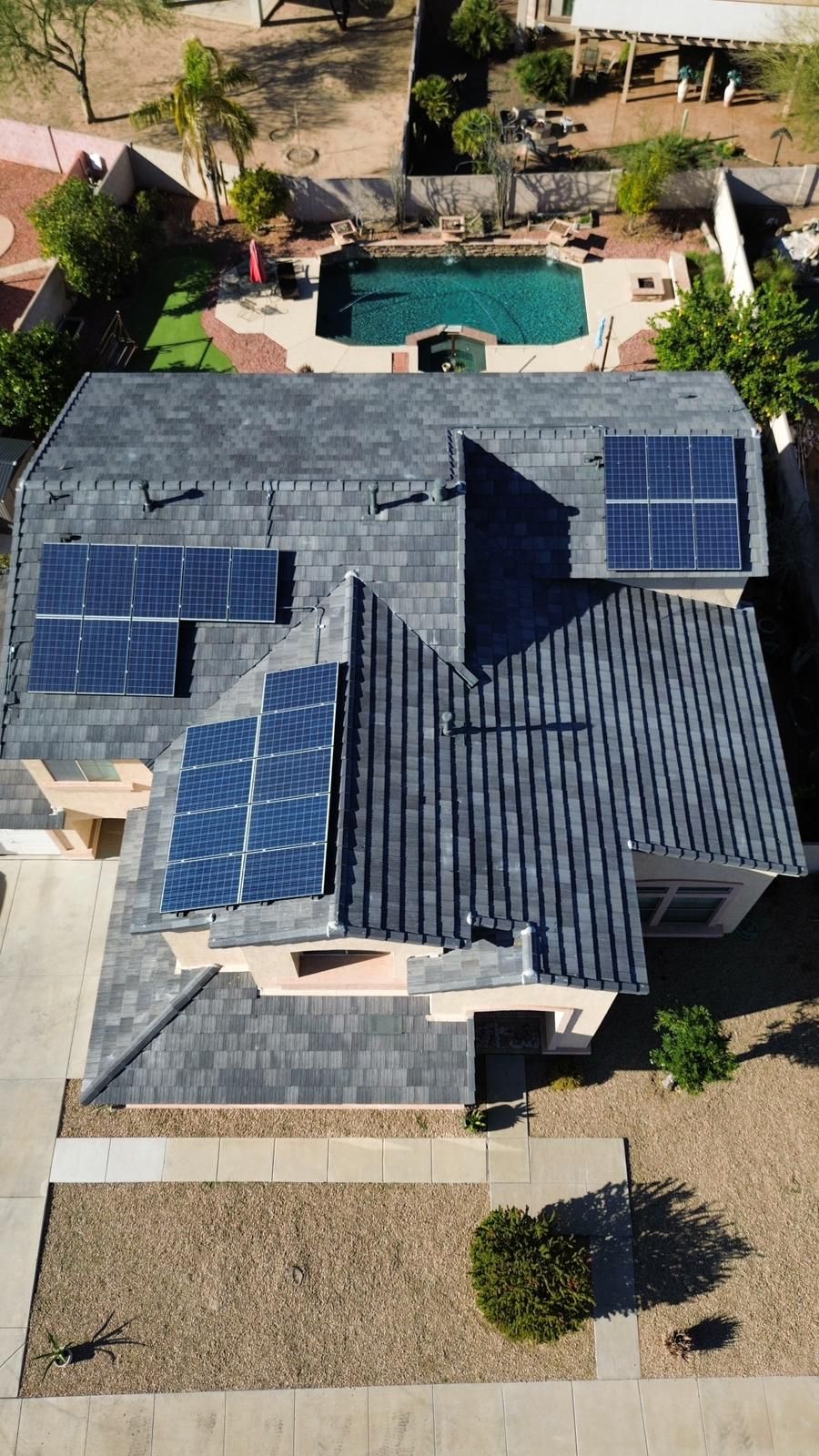 Overhead view of a house with solar panels on a dark gray roof.  A pool and backyard are visible.