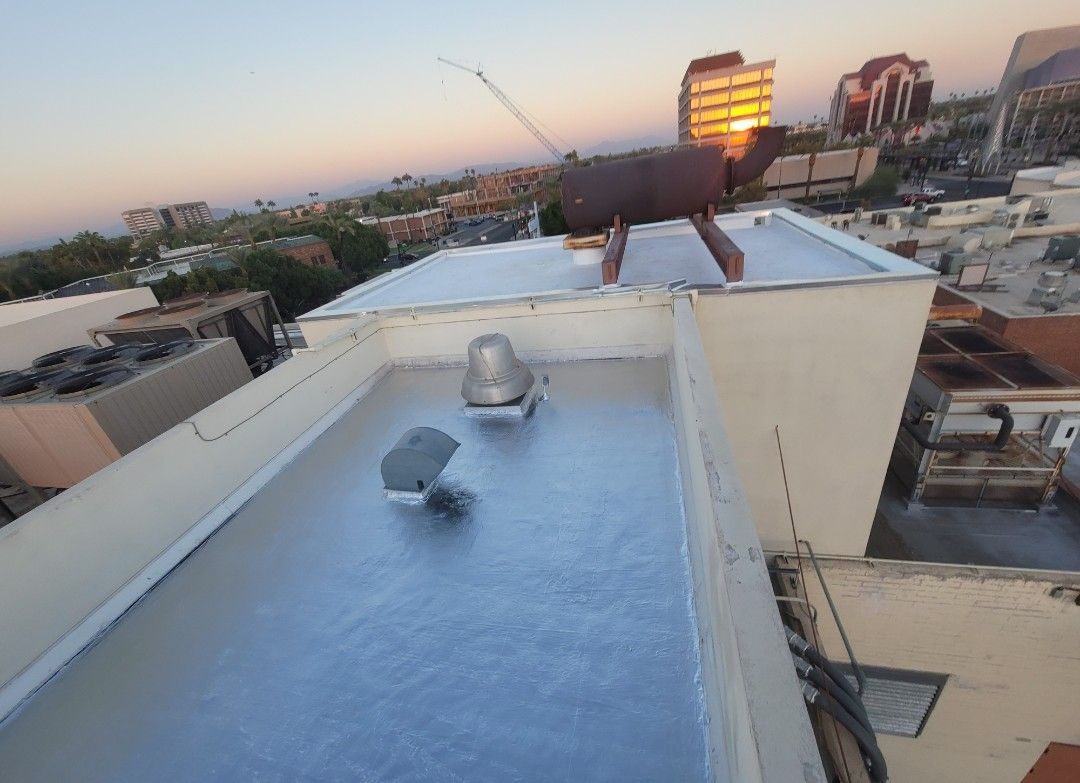Rooftop with reflective silver coating, vents, and a person walking towards the edge, sunset in the background.