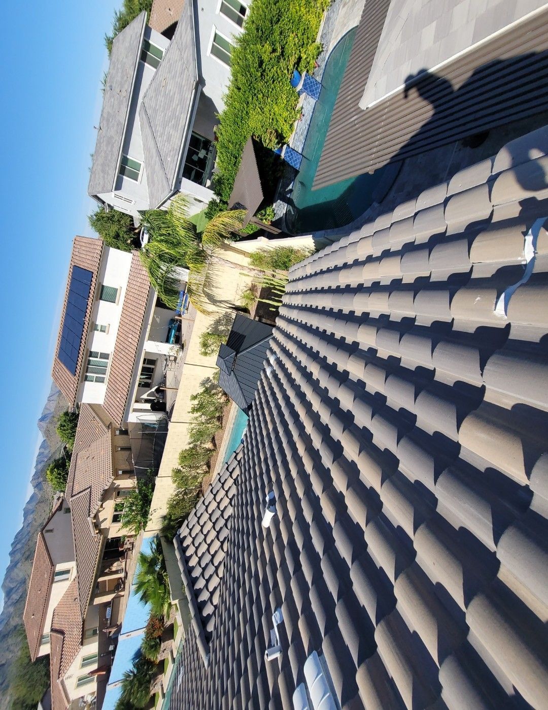 View from a tile roof overlooking suburban homes, pool, and green vegetation on a sunny day.
