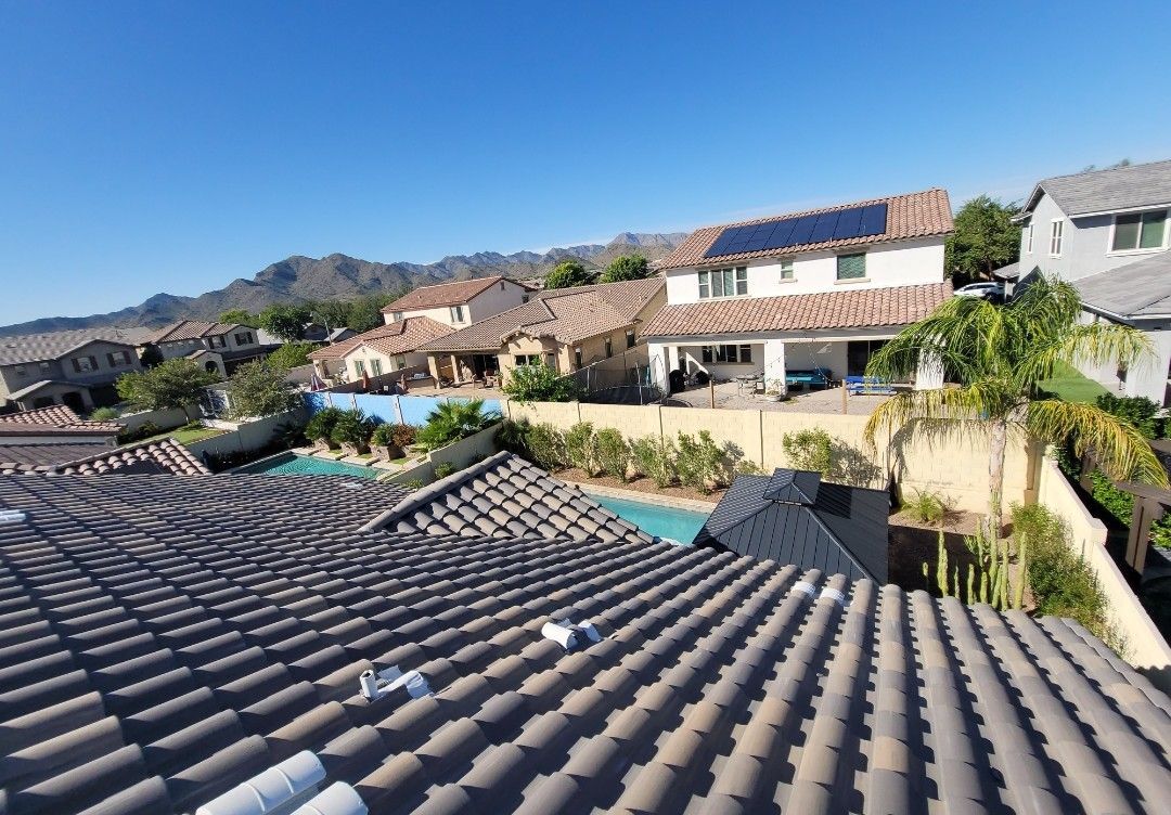 Rooftop view of houses with tile roofs, a pool, and solar panels against a blue sky.