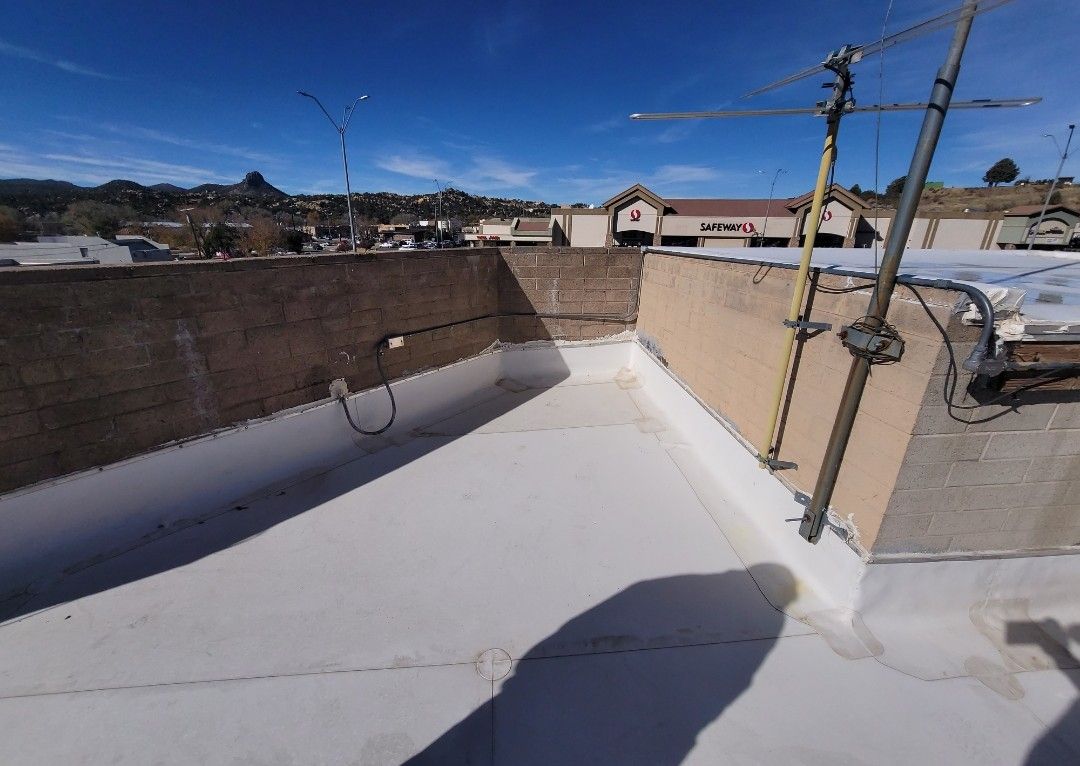 Flat roof with white coating, beige walls, clear blue sky, buildings in the background.