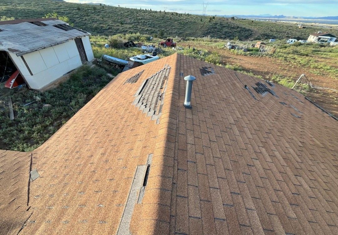 Gray asphalt shingle roof with a stone chimney; some shingles are missing.
