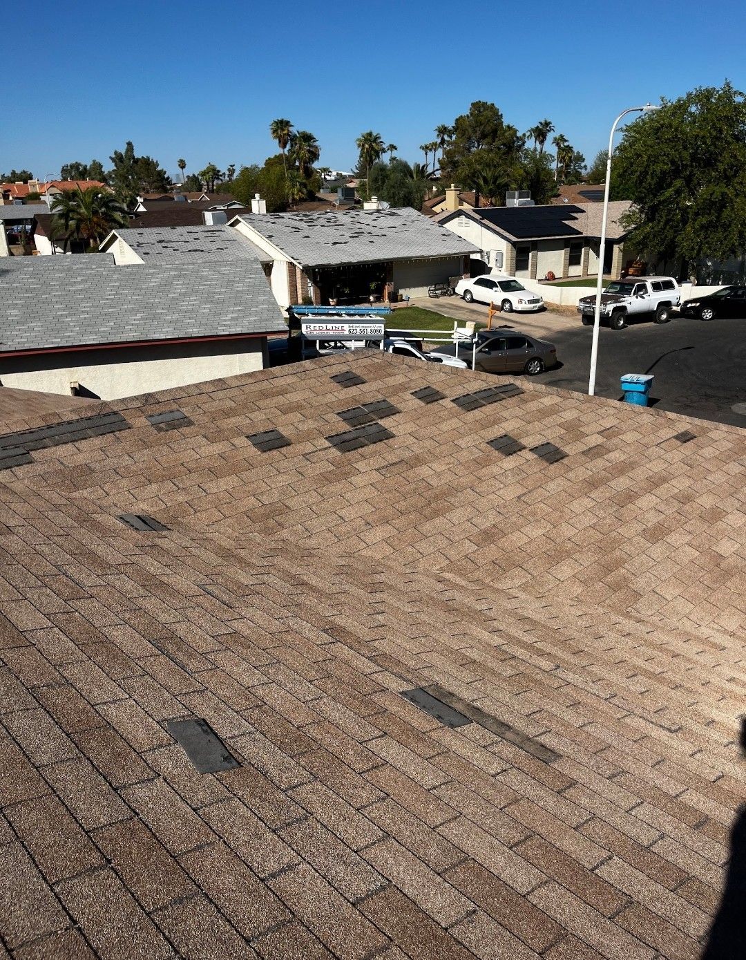 Rooftop with missing shingles, view of neighborhood houses under a bright blue sky.