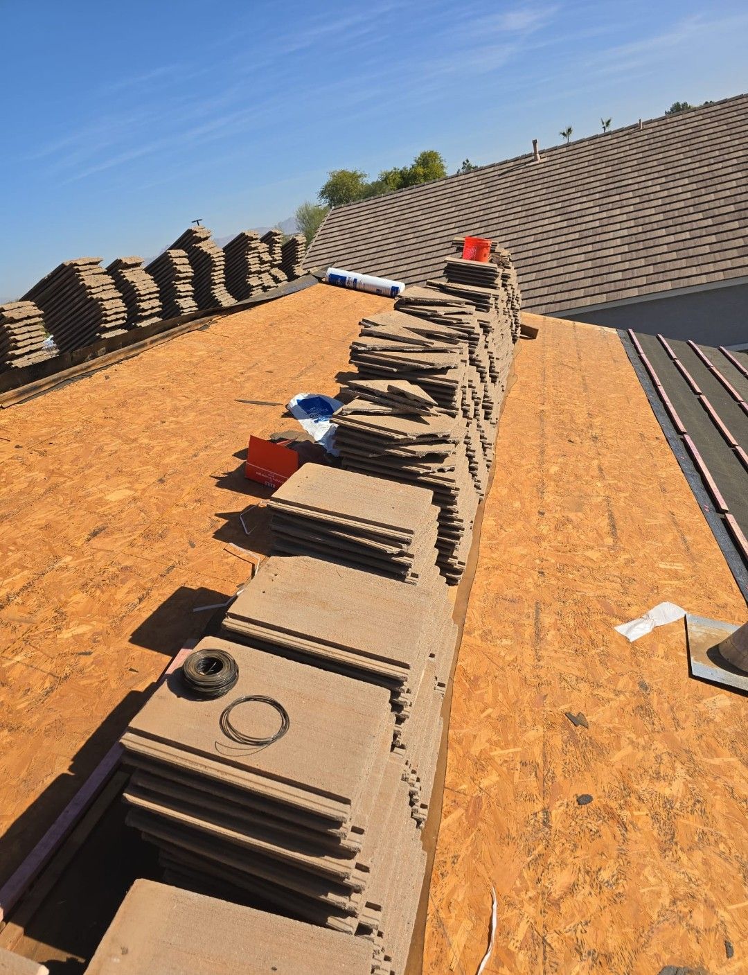 Roofing materials stacked on a partially completed rooftop, clear blue sky.