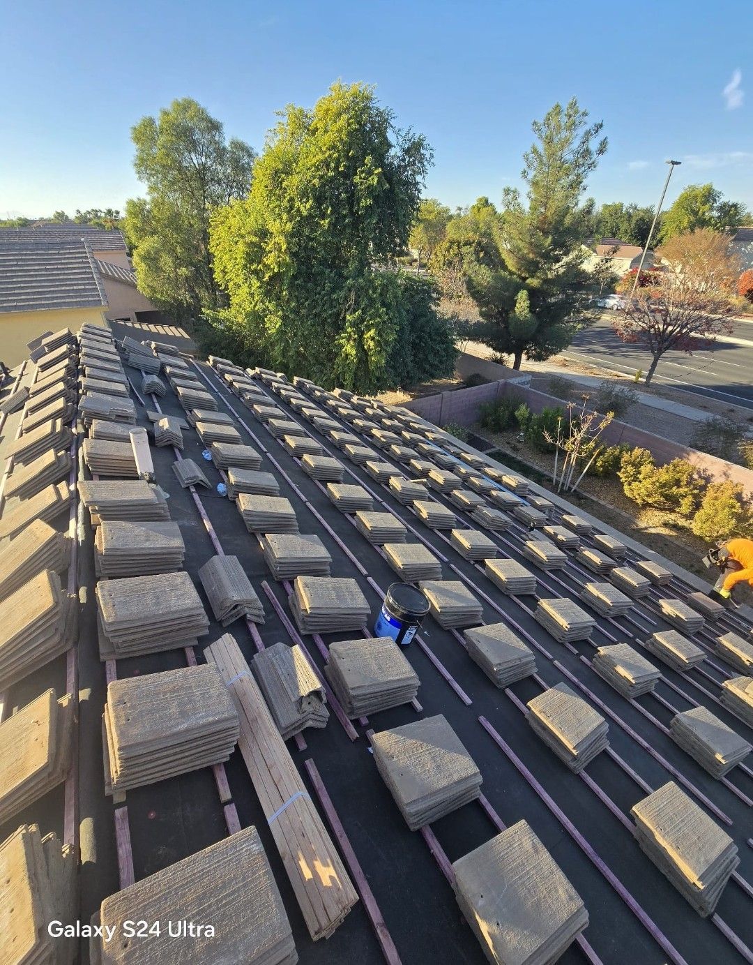 Roof tiles laid out on a roof with trees and a clear sky in the background.