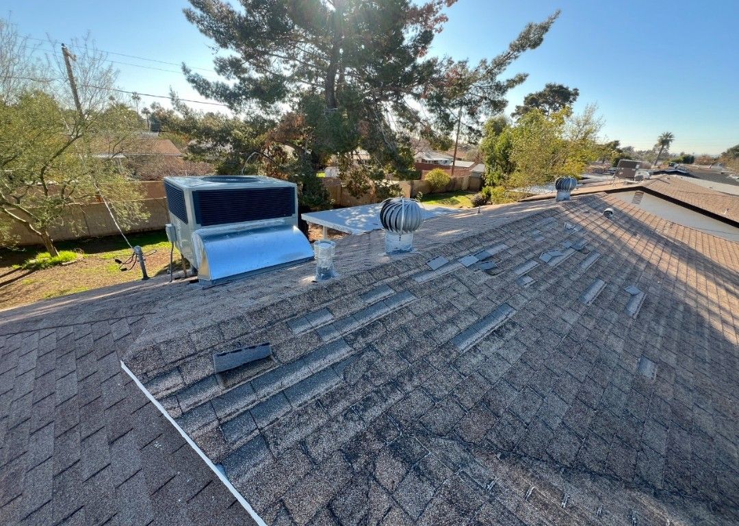Rooftop view with AC unit, vent, and weathered shingles. Sunny day with trees and houses in the background.
