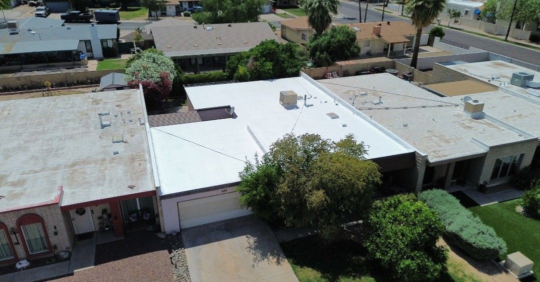Aerial view of residential homes with white and gray flat roofs and surrounding trees.