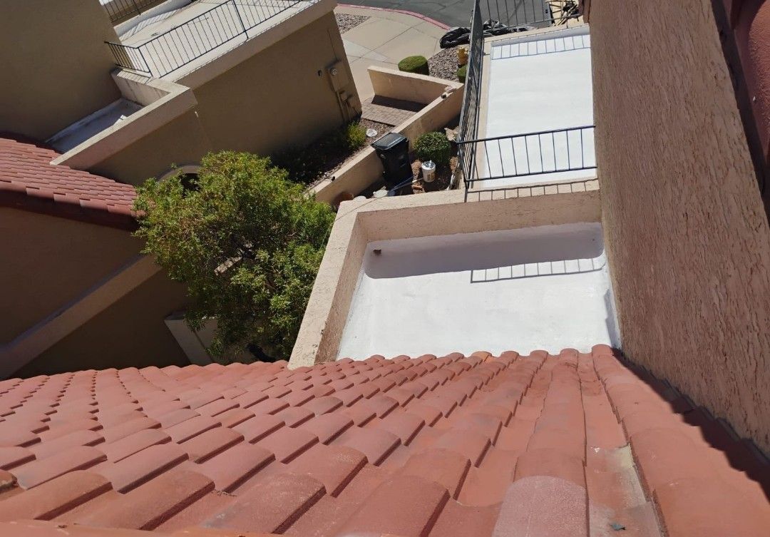 Looking down from a terracotta tile roof towards a complex of buildings with white walls and a small tree.