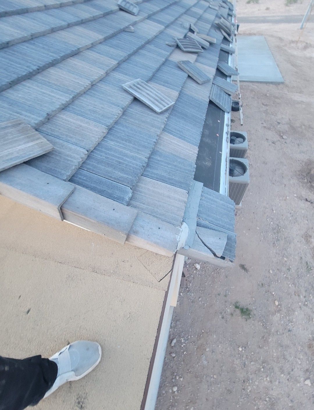 Damaged blue tile roof with several displaced tiles, corner view.