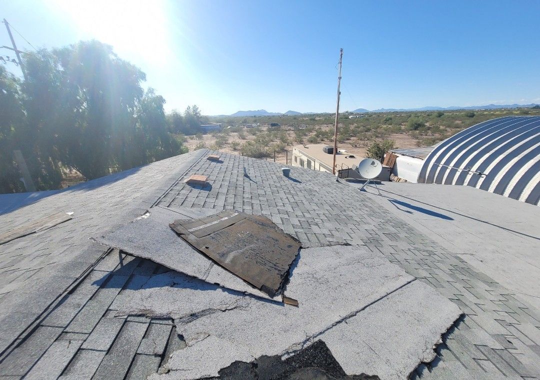 Damaged asphalt shingle roof on a sunny day. Desert landscape in the background.