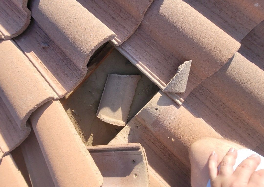 Close-up of a damaged terracotta tile roof with broken and missing tiles, showing the underlying structure.