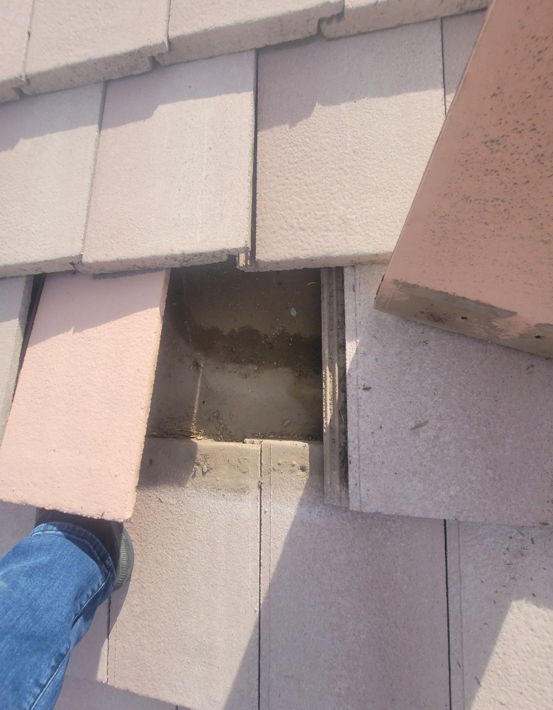 A roof with missing tiles exposing a square opening; a person's foot is visible.