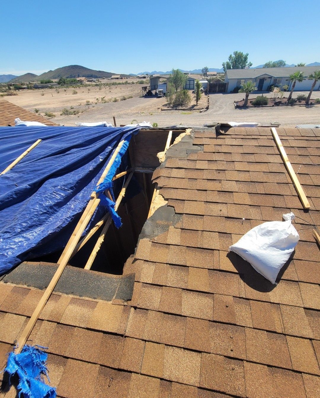 Roof with a large hole covered by a blue tarp, white bag, and distant desert landscape.