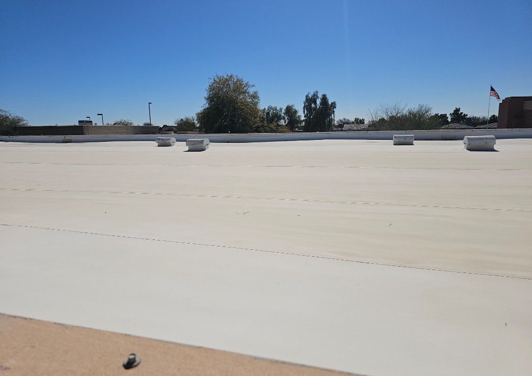 Flat white roof with vents, trees, and a blue sky.