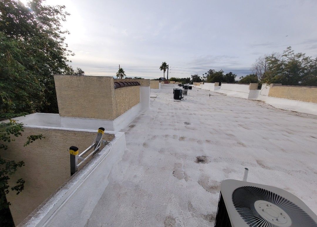 White-coated flat roof with HVAC units, chimney, and surrounding trees under a cloudy sky.