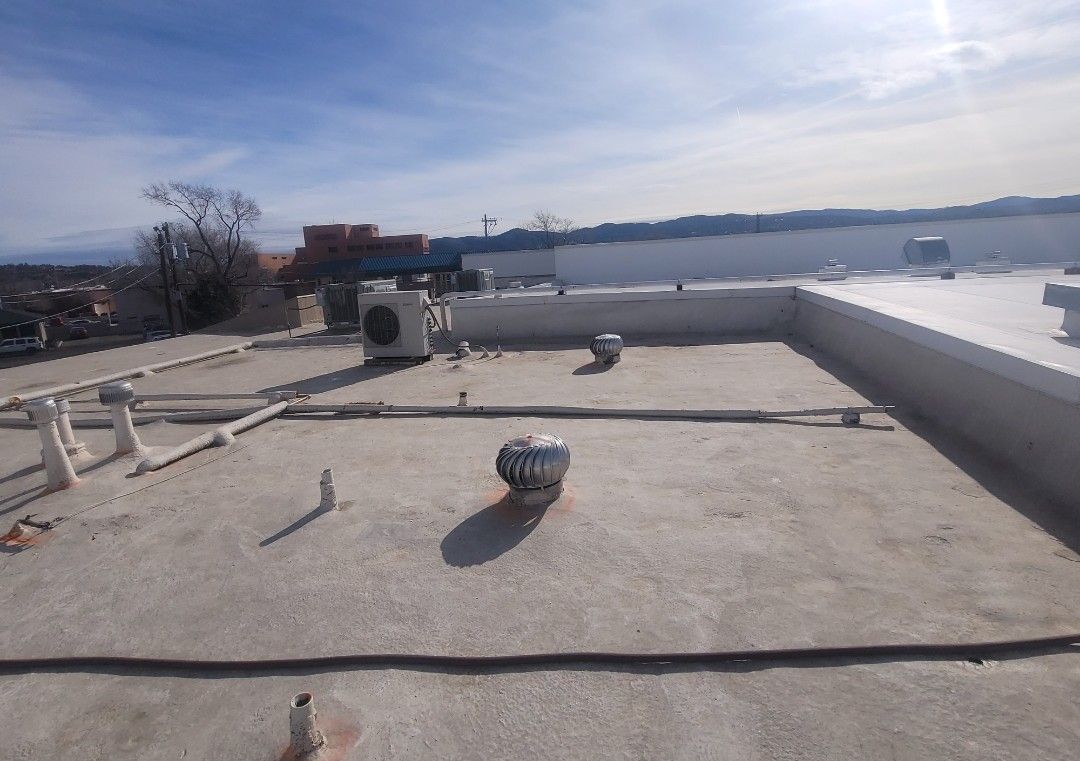A flat commercial roof with equipment. Gray, white, and blue tones dominate the sunny scene.