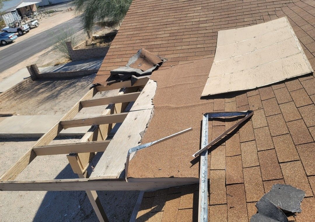 Rooftop with missing shingles and exposed wooden structure, near a road.