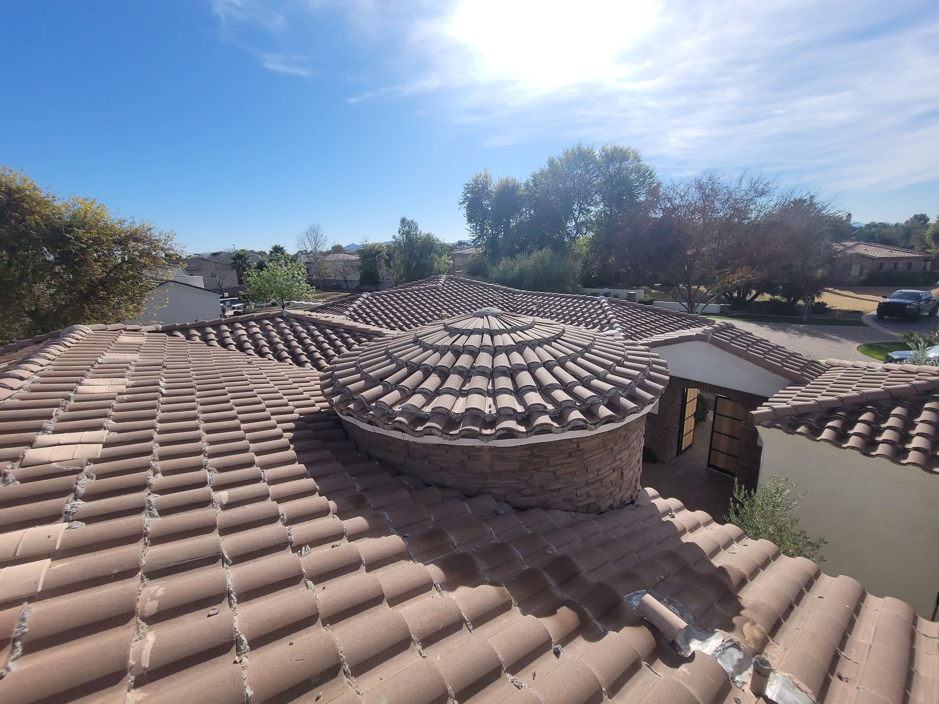Tiled roof with a circular structure on a sunny day. Trees and houses visible in the background.
