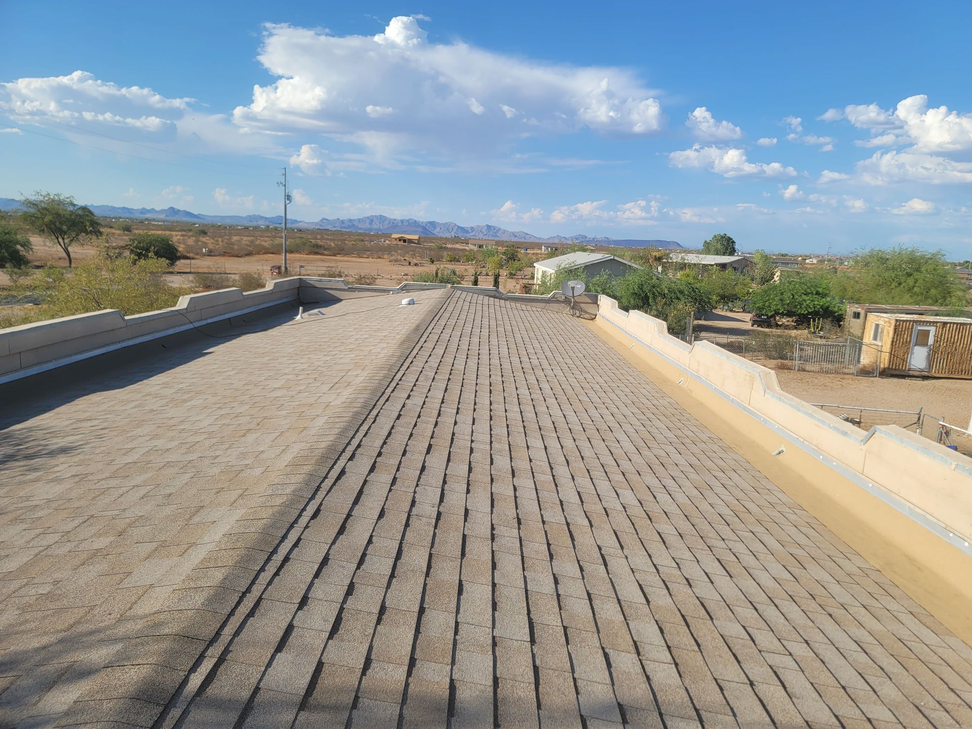 Gray shingle roof with two dormers: one metal, one shingled. Clear, sunny sky.