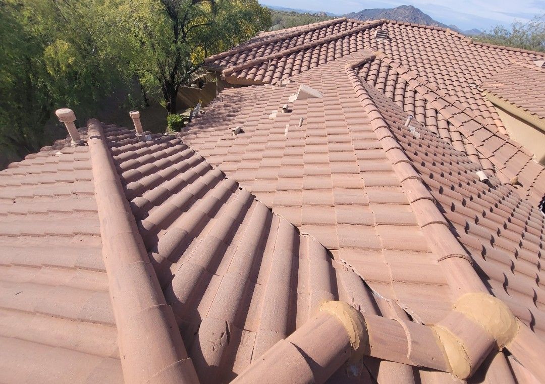 Clay tile roof with ridges, vents, and valleys in brown hues against a natural setting.
