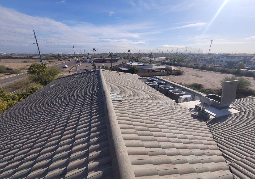 View from a rooftop with tile roofing, looking towards a road, buildings, and a clear blue sky.