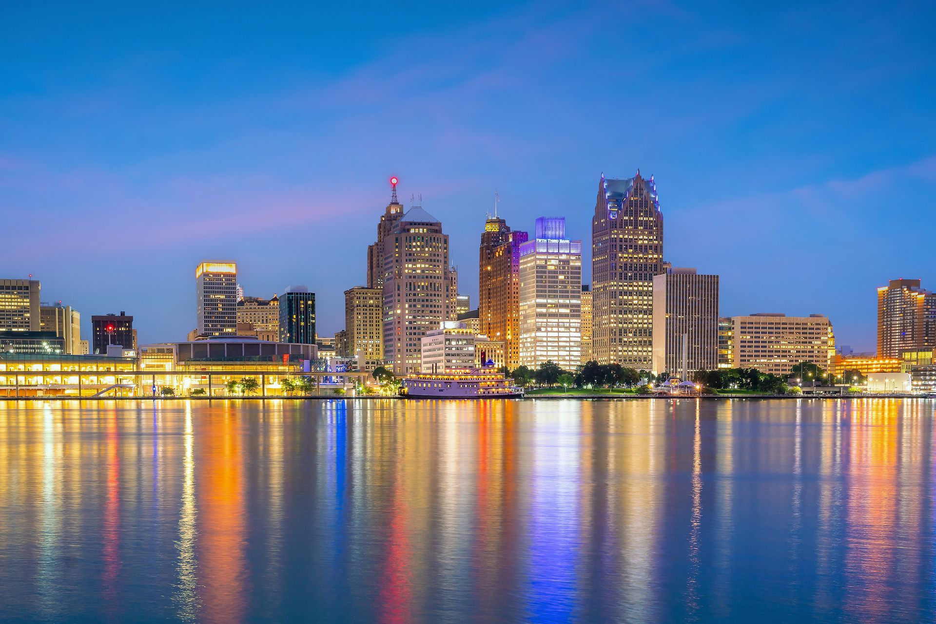 Detroit skyline at dusk with colorful building lights reflected on calm water