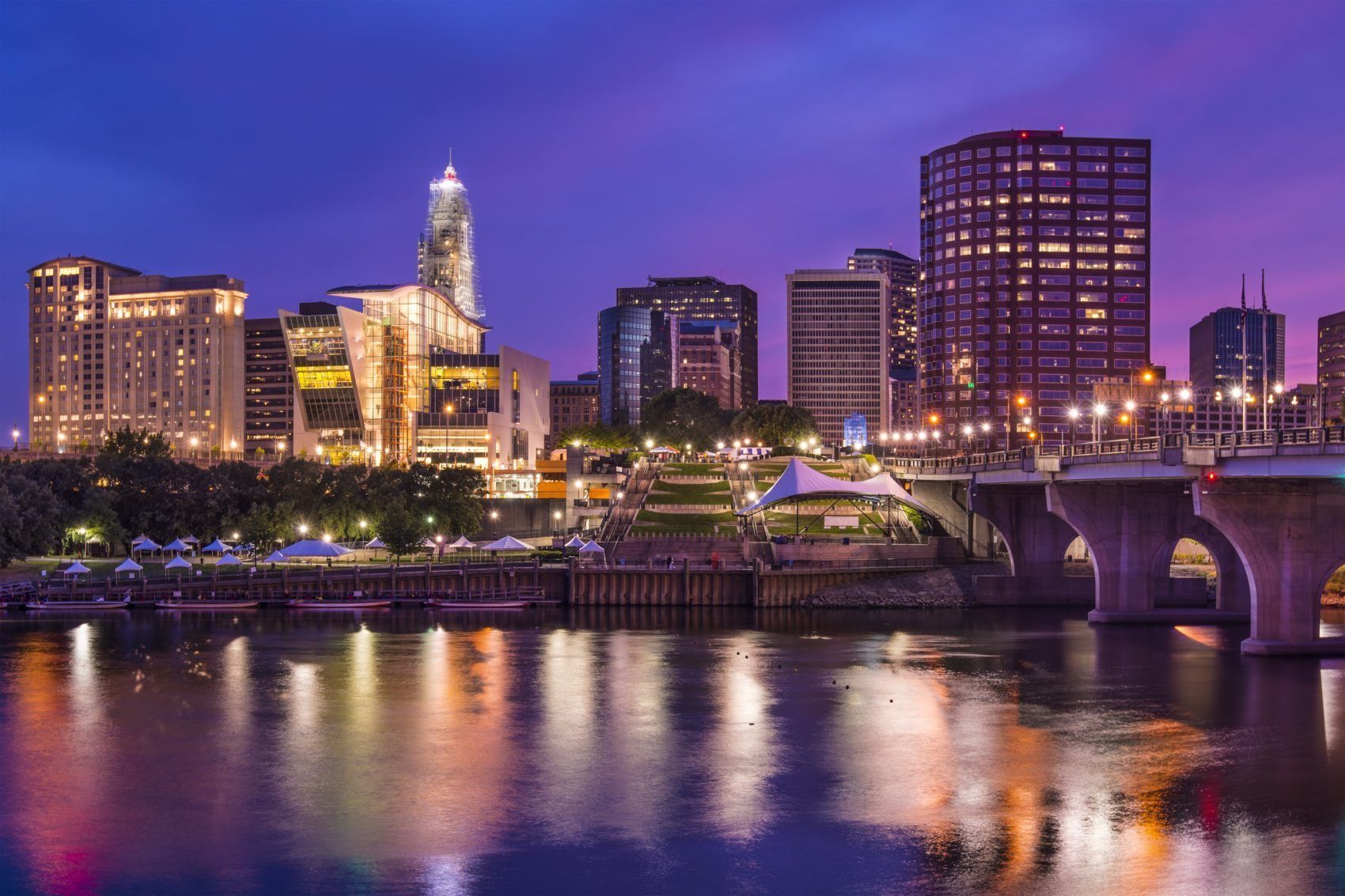 City skyline at dusk reflecting in a river, purple and orange hues.
