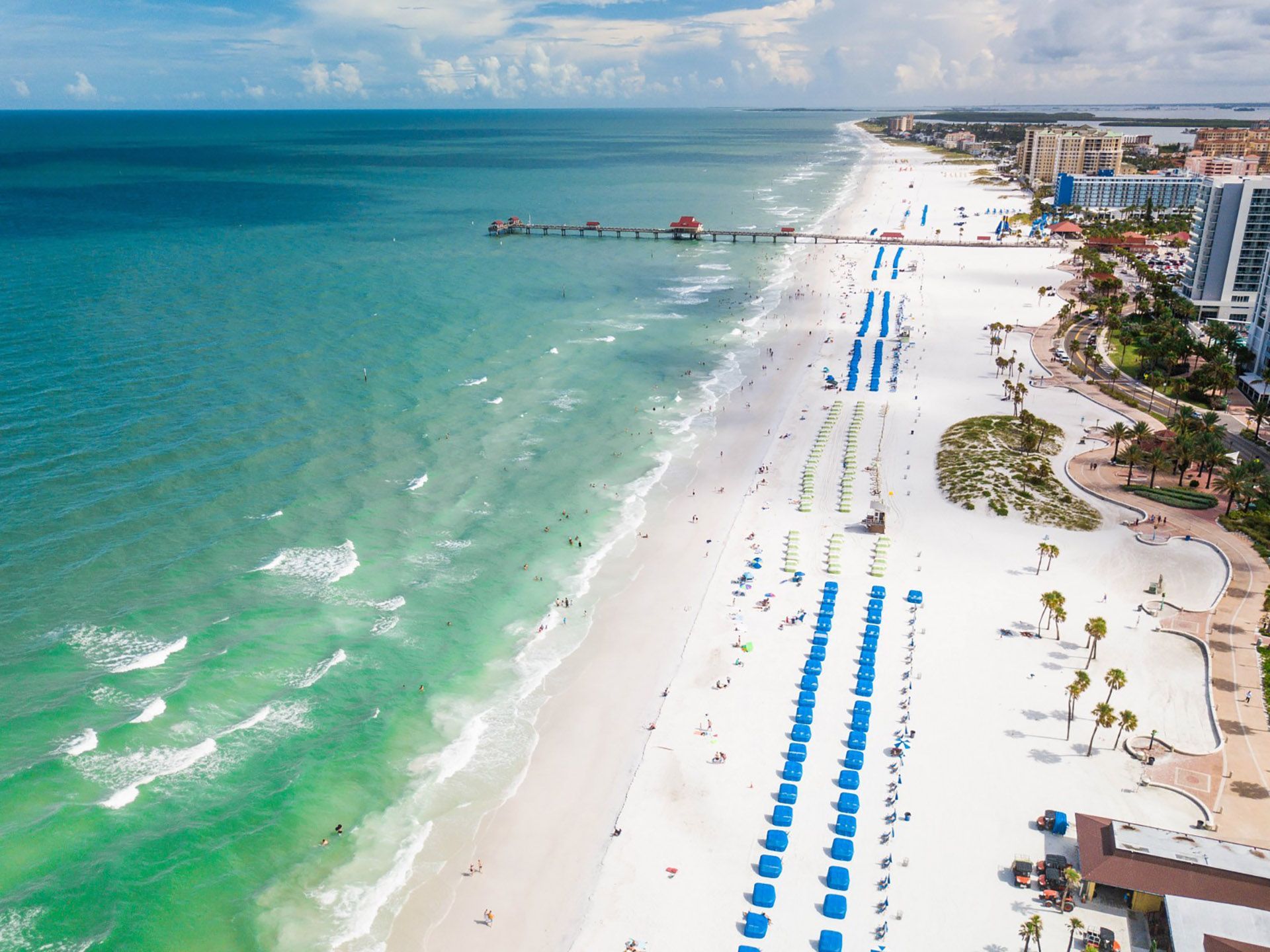 Aerial view of Clearwater Beach in Florida; white sand, turquoise water, blue umbrellas, pier, and buildings.
