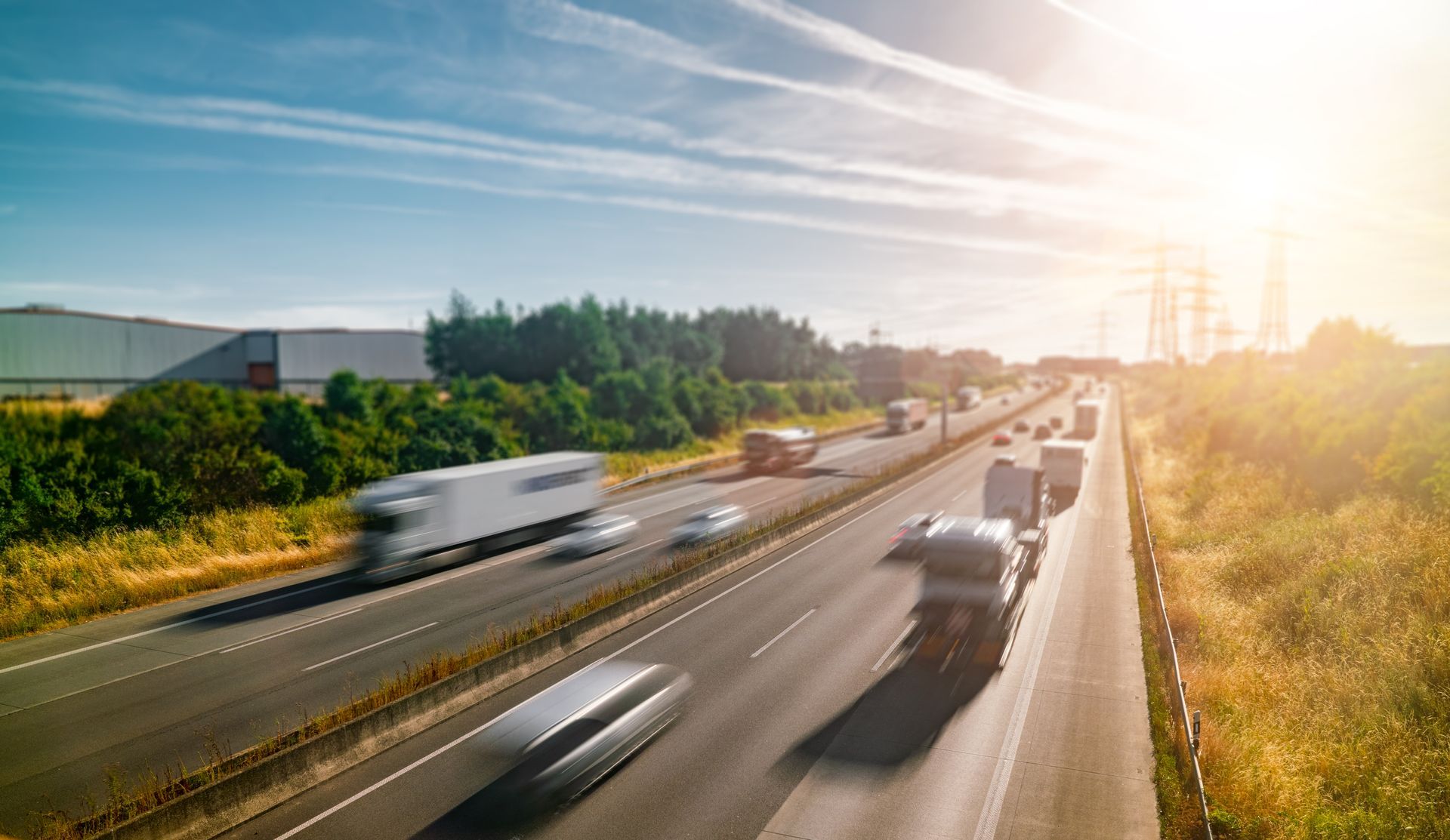 Highway with traffic on a sunny day. Trucks and cars moving, with grassy fields and trees beside the road.