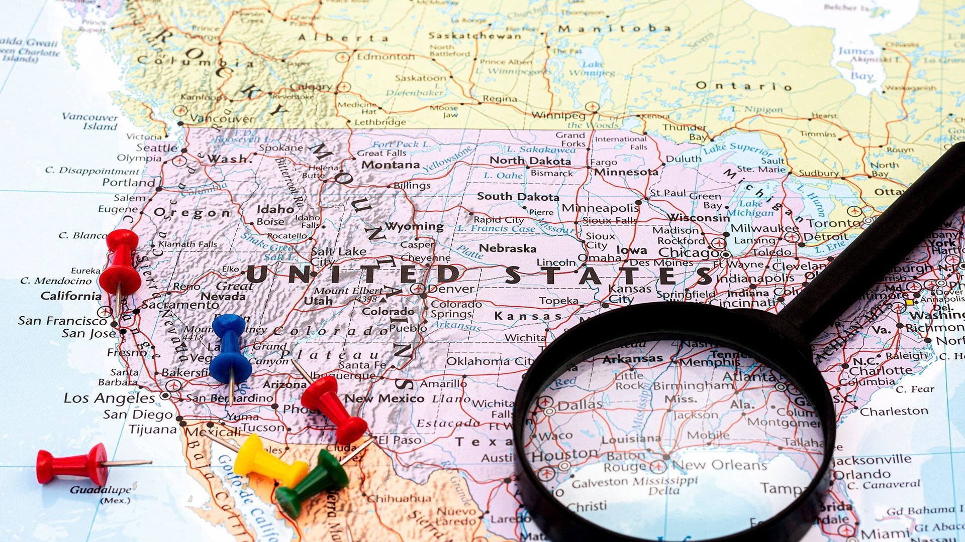 Map of the United States with colorful push pins and magnifying glass.