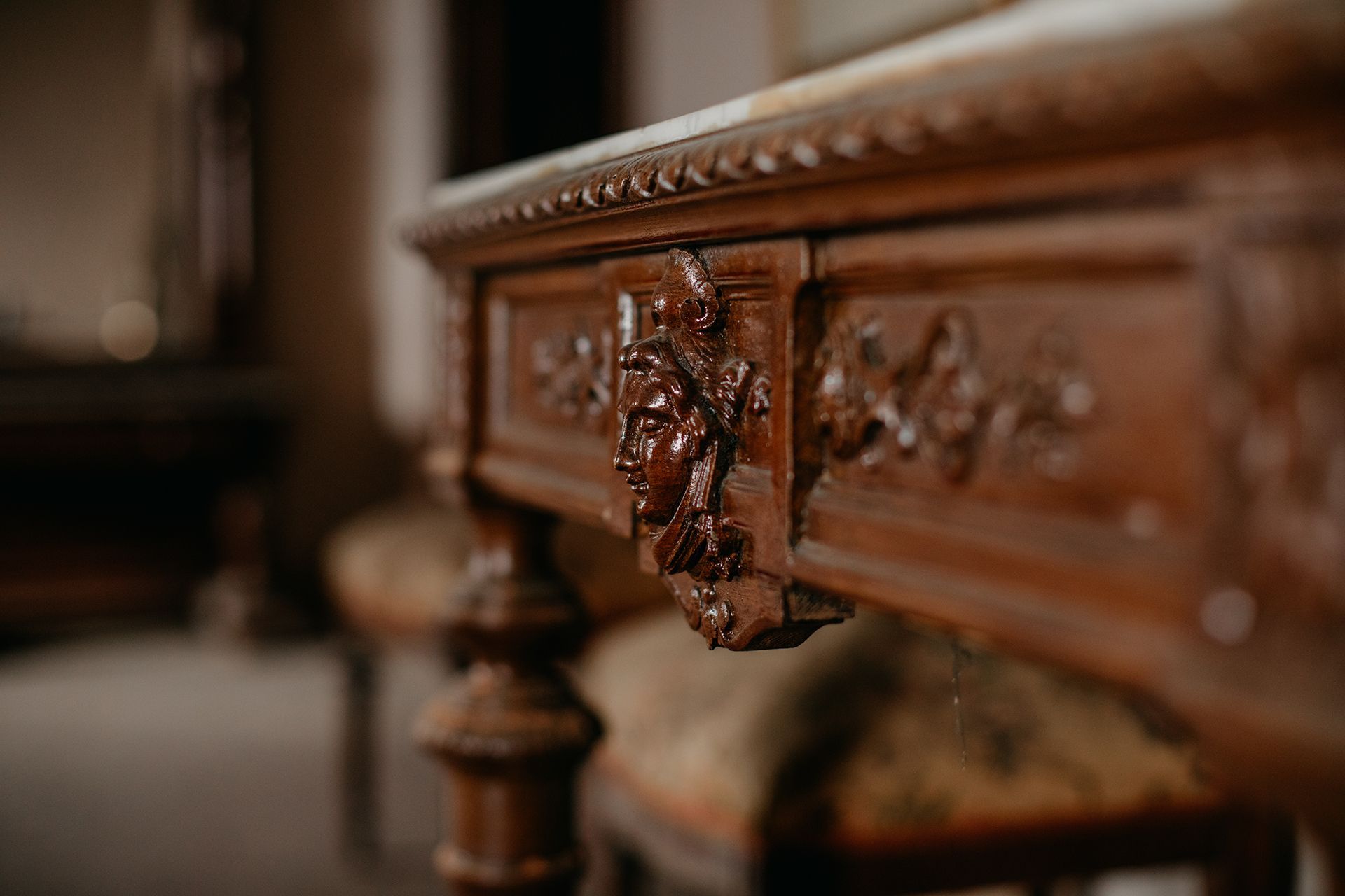 Close-up of a richly carved antique wooden table. Ornate floral details and turned legs are visible.