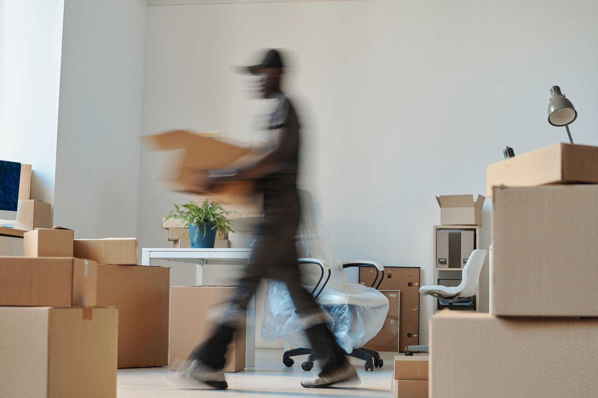 Man carrying a cardboard box in a room filled with moving boxes.
