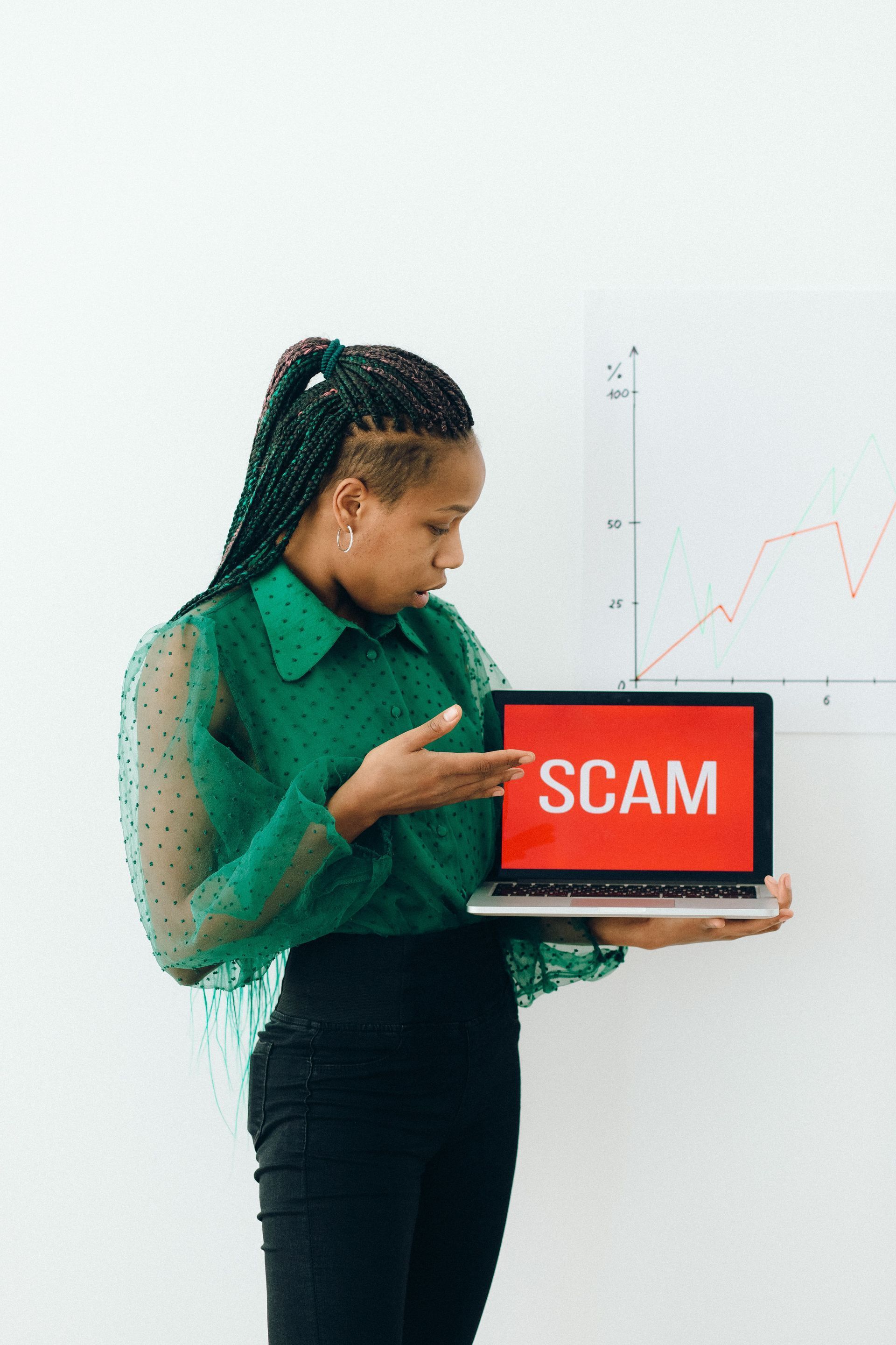 Person holding a laptop with “SCAM” on the screen in a bright office setting