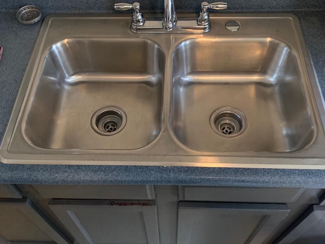Stainless steel double kitchen sink with faucet, mounted in a blue countertop over a cabinet.