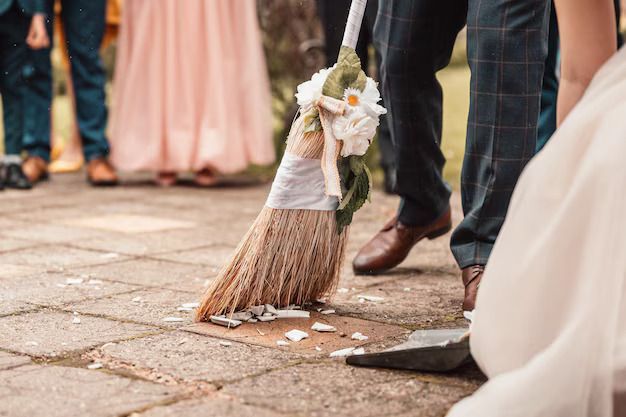 Bare feet sweeping gold confetti with a broom and dustpan on a wooden floor.