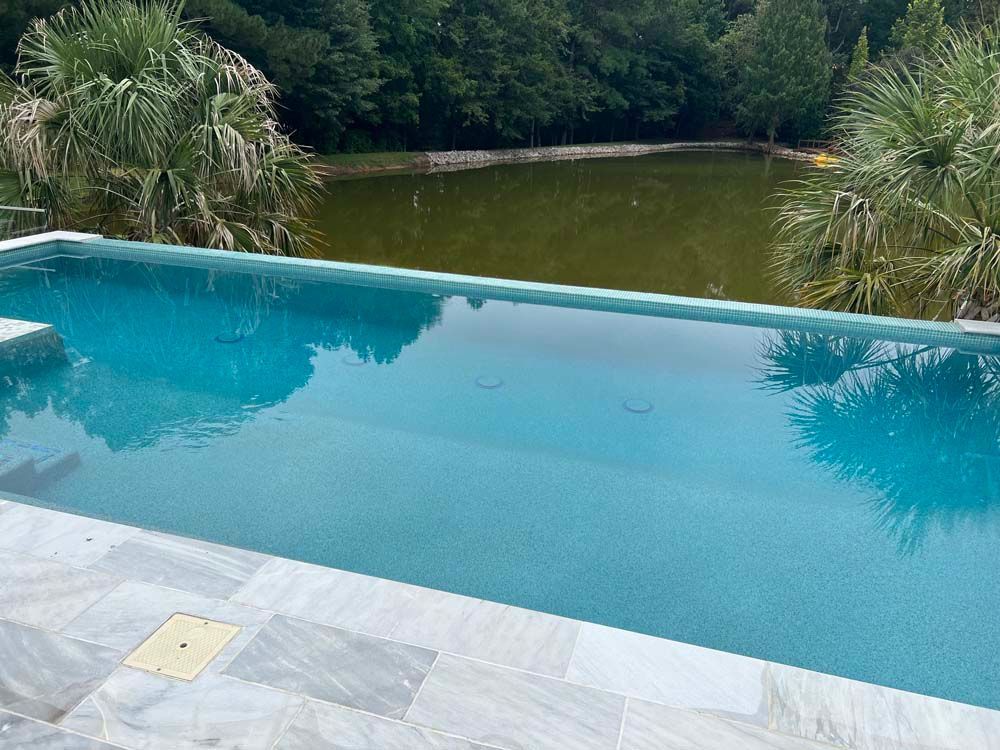 Infinity pool with blue water overlooking a green pond and trees.